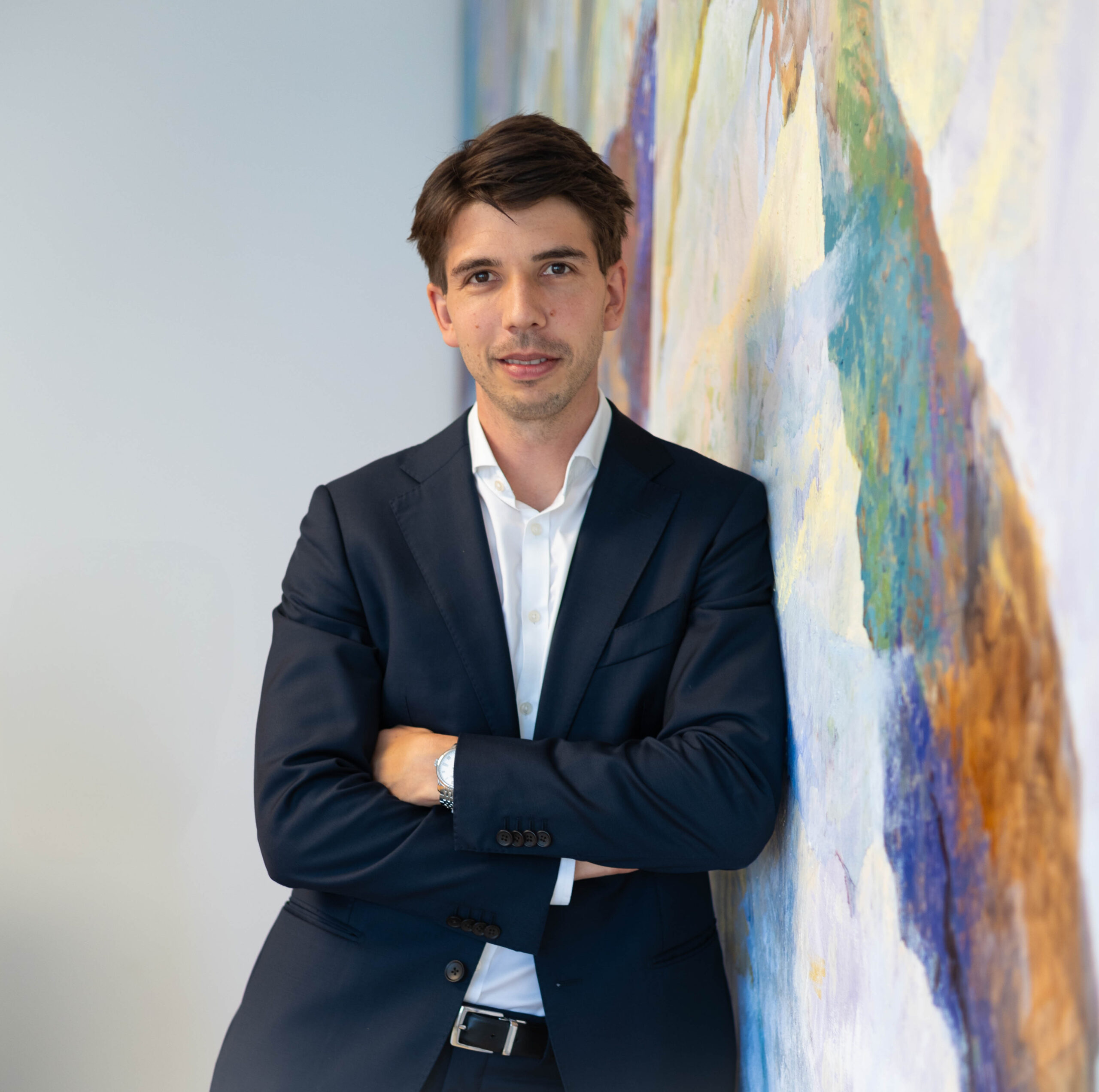 Philipp Horvath lehnt an einer Wand, die Hände locker verschränkt. Er hat braune Haare und einen Anzug an.